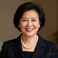 一位气质优雅的女士半身照，穿着深色套装，戴着珍珠项链，面带赞许的微笑